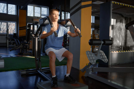 Athletic teenage boy enjoying hard training on fitness machine at gymの写真素材