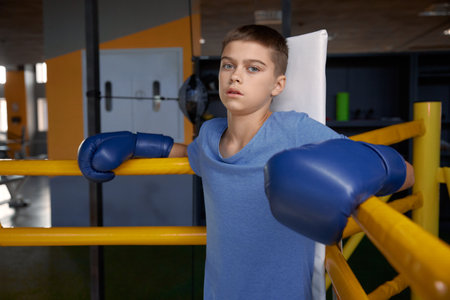 Teenage boy boxer wearing gloves inside boxing ring posing for cameraの写真素材