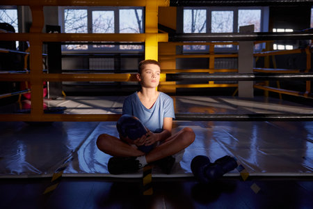 Teenage boy boxer resting after training inside boxing ring posingの写真素材
