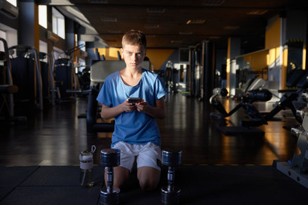 Teen boy with phone searching training video tutorial for sport activity at gymの写真素材