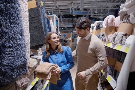 A cheerful woman joyfully embraces soft textiles as a man evaluates various products in a home storeの写真素材