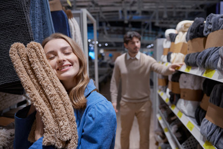 A cheerful woman joyfully embraces soft textiles as a man evaluates various products in a home storeの写真素材