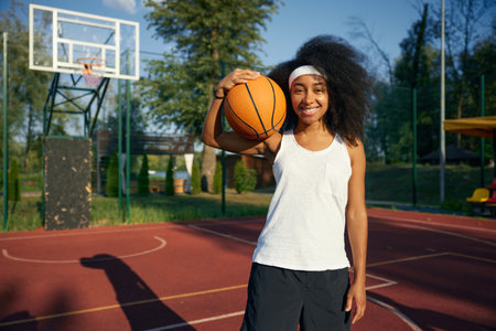 Smiling teenage girl basketball player with ball over outdoor court backgroundの写真素材