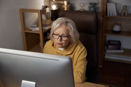 Focused elderly woman using desktop computer at home portrait shot