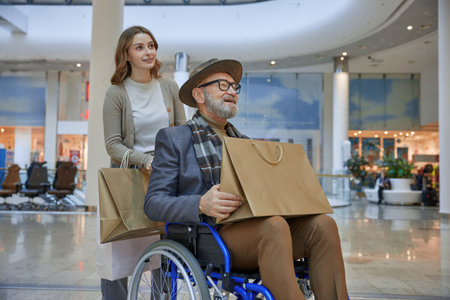 Man in a wheelchair is assisted by a woman in a mallの写真素材