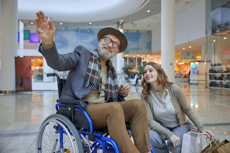 A man in a wheelchair sits beside a woman with shopping bagsの写真素材