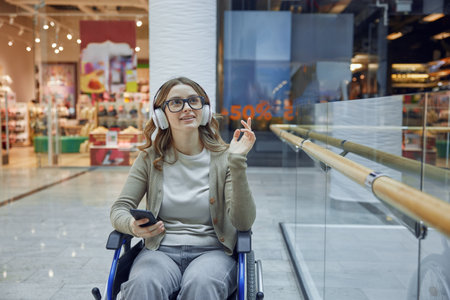 A young woman enjoying music while relaxing in her wheelchair at a busy mallの写真素材