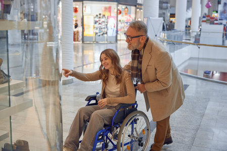 Family moment at shopping mall, mature granddad helping his granddaughter in a wheelchairの写真素材