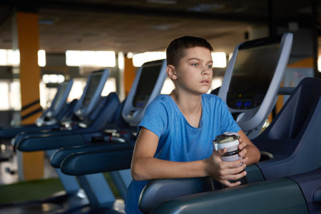 Pensive tired boy relaxing after cardio training on treadmill at sport clubの写真素材
