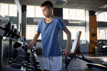 Teenage boy choosing dumbbell weight for training workout at gymの写真素材