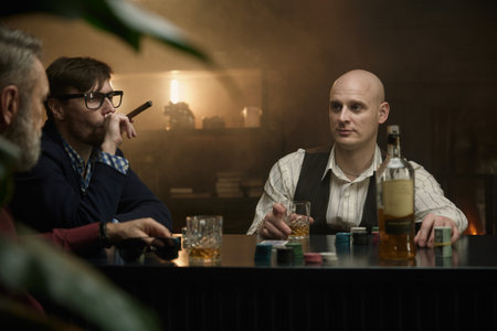 A group of men enjoying time playing poker in a dimly lit bar while sipping on drinksの写真素材