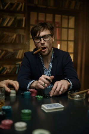 Man holding a cigar at a poker table with alcohol drink nearby