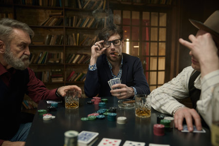 Male friends company playing cards in a dimly lit bar while sipping on drinks