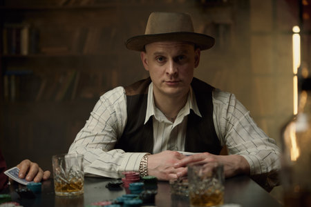 Man dressed in vintage attire at a dimly lit, smoky table while playing pokerの写真素材