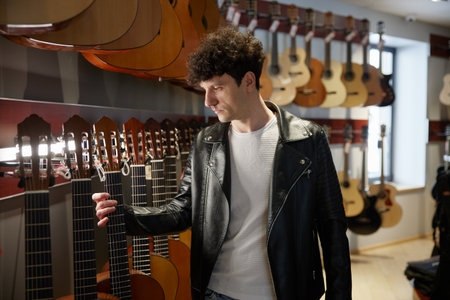 A man in a stylish leather jacket holds an acoustic guitarの写真素材