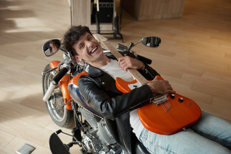 A young and talented musician taking some time to relax casually with his guitar on a motorcycleの写真素材
