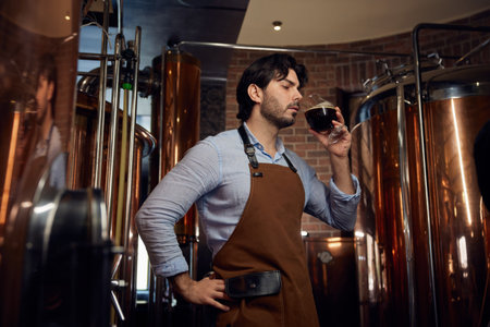 Brewer wearing an apron and is holding a glass filled with fresh beer