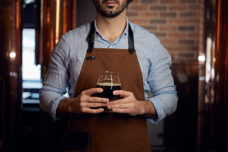 A man wearing an apron is holding a frosty glass of beer