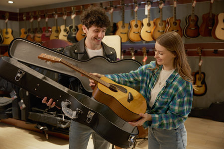 Man and woman is holding a guitar in front of a wall of guitars