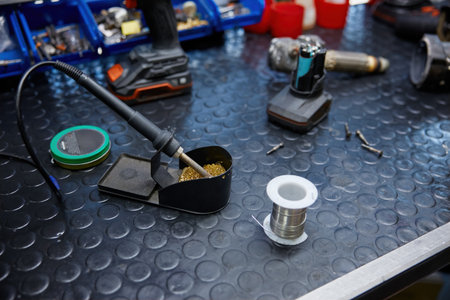 A soldering iron is resting on a worktable with a soldering iron and solder