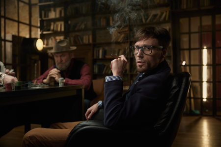 Stylish man playing poker with his partners in a mysterious setting while smoking a cigar