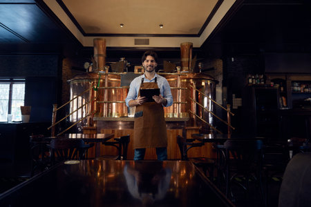 Brewer man dressed in an apron is standing in brewery