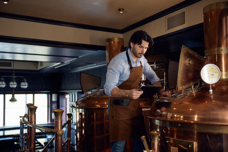 Brewer wearing an apron is diligently working on a copper machine
