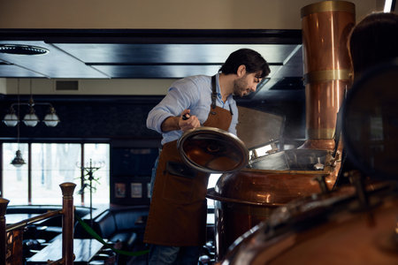 Brewer man wearing an apron is diligently working on a copper machine