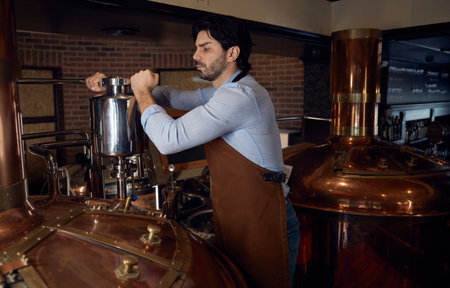 Brewer man wearing an apron is diligently working in a brewery setting
