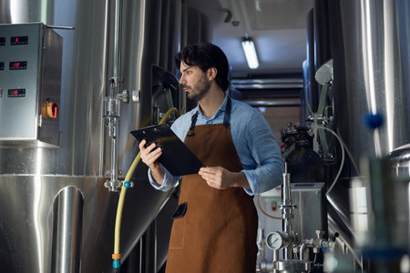 A man wearing an apron is utilizing a clipboard in a factory settingの写真素材