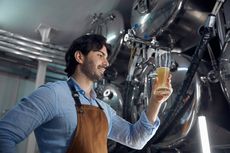 A man is holding a glass of beer while inside a brewery settingの写真素材