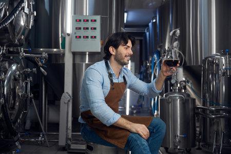 A man sits on a stool in a brewery holding a beer glassの写真素材