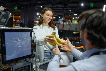 A woman is giving a banana to a man cashier at a grocery store