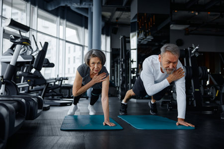 Mature man and woman are doing exercises on yoga mats in a gymの写真素材