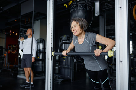 An older woman is performing push ups on a specialized machine in a gymの写真素材