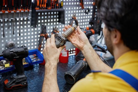 Service man repairing a broken power drill inside a busy workshopの写真素材