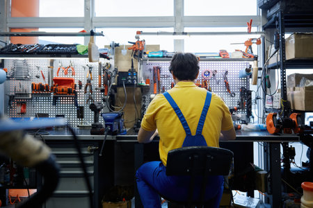 A man worker in work clothes sits at a workbench