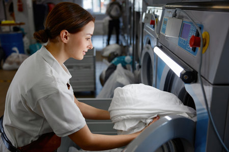 A woman wearing a white shirt is diligently working in a laundromatの写真素材