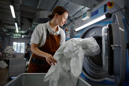 A woman is in the process of putting various clothes into a washing machineの写真素材