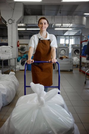 Female worker pushes a cart full of laundry in a laundromatの写真素材