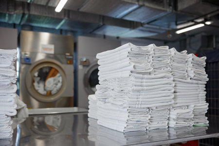 A stack of clean towels is on a table in front of a washing machineの写真素材
