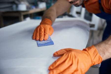 Craftsman sanding surfboard in workshop with hands with orange gloves finishing boardの写真素材