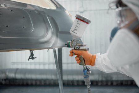 A technician spray-painting car hood inside a controlled automotive spray boothの写真素材