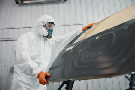 A technician in a protective suit works on a car panel in a safety-focused spray boothの写真素材