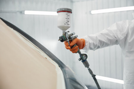 A technician carefully spraying high-quality automotive paint on a car door in a white garageの写真素材
