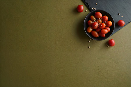 Cherry tomatoes in black bowl on green background with copy space.の素材
