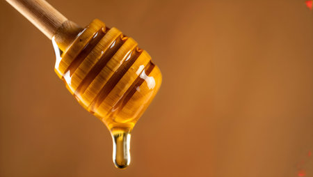 Honey dripping from a wooden honey dipper on a brown backgroundの素材
