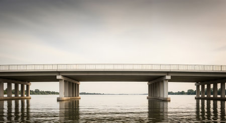 Concrete bridge spanning over tranquil water scene. Minimalist design and horizontal lines emphasize architecture. Calm water reflects the sky, peaceful backdrop.の素材