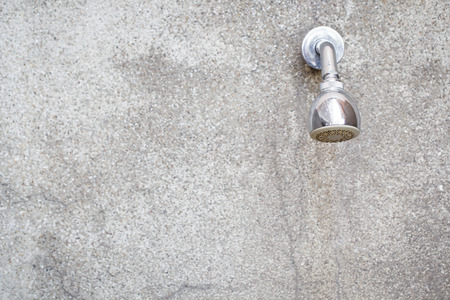 Outdoor shower head set up on concrete wall beside a swimming.
