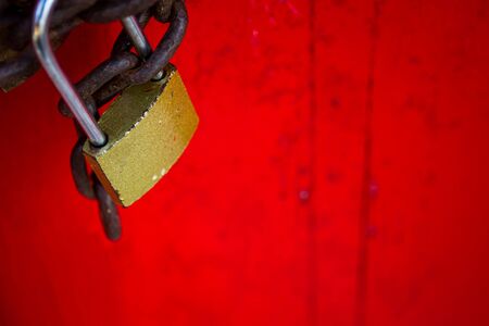 Old lockpad locked on a wooden red door with rusty chain close up background.の写真素材